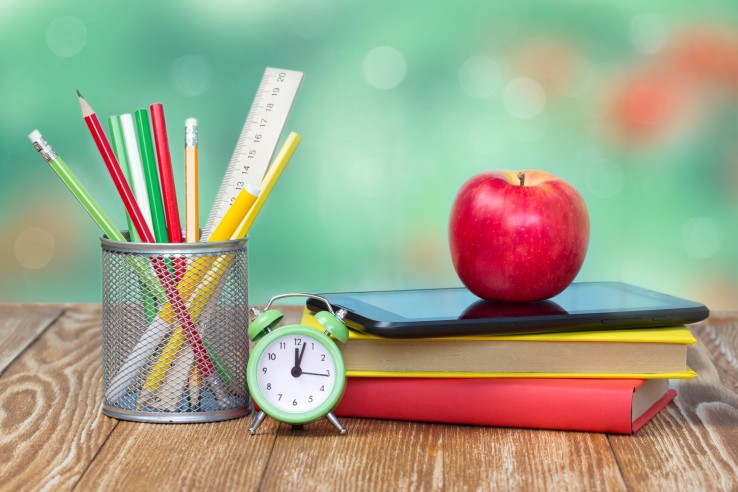 School supplies on wooden table desk nature green background empty space.Apple stack books stationary alarm back to school concept.
