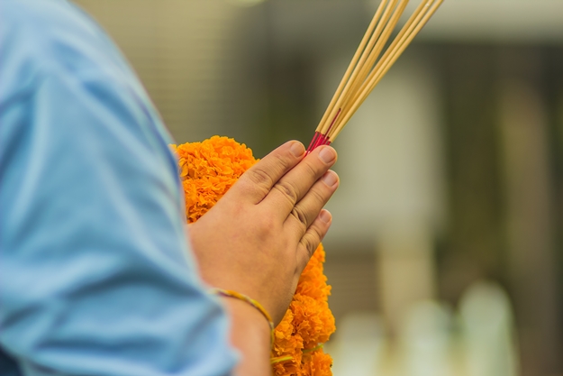 Close up people hands holding incense sticks and marigold, flower wheel during made merit for worship ceremony