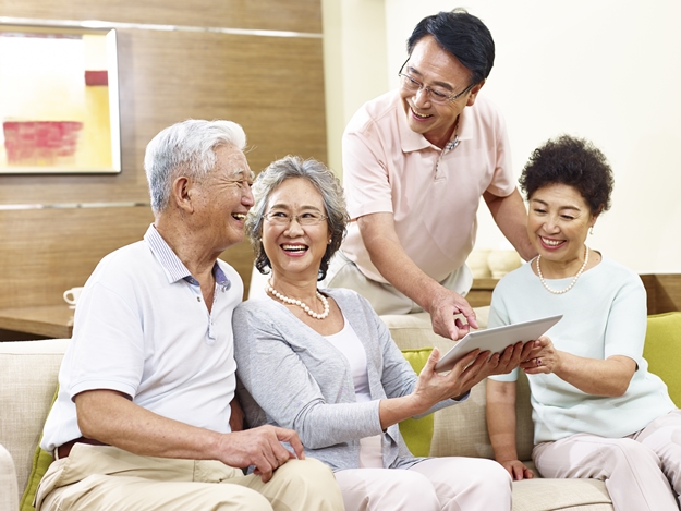 two active senior asian couples looking at tablet computer, happy and laughing