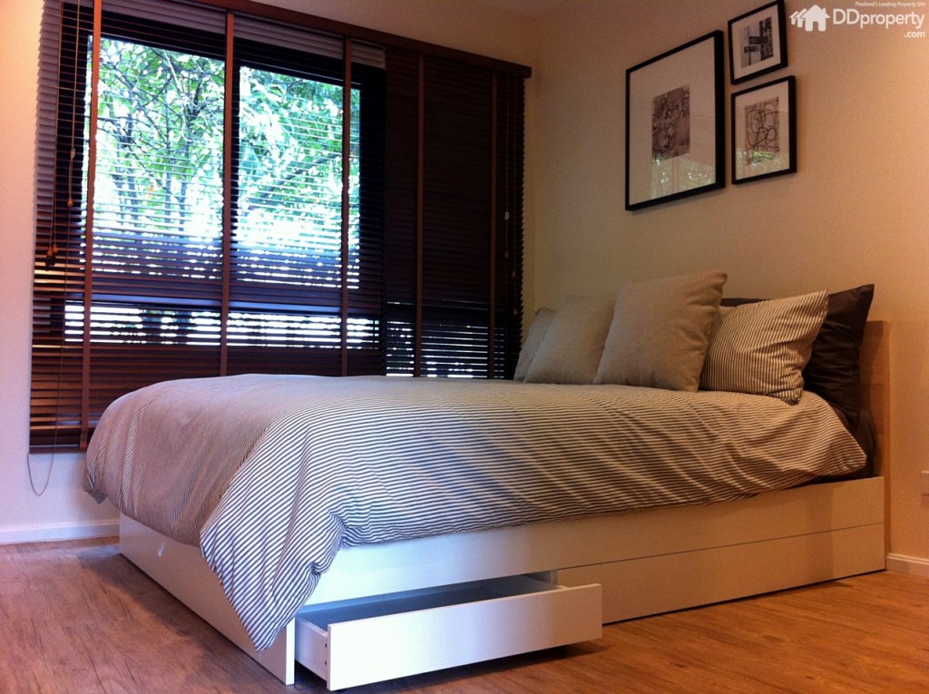 ห้องนอนกรุกระจกบานใหญ่เพิ่มความโปร่งให้แสงธรรมชาติเข้าถึง บิลท์อินเตียงขนาด 5 ฟุต สีขาว ตัวเตียงมีลิ้นชักเป็นลูก้เล่นสำหรับเก็บของด้วย