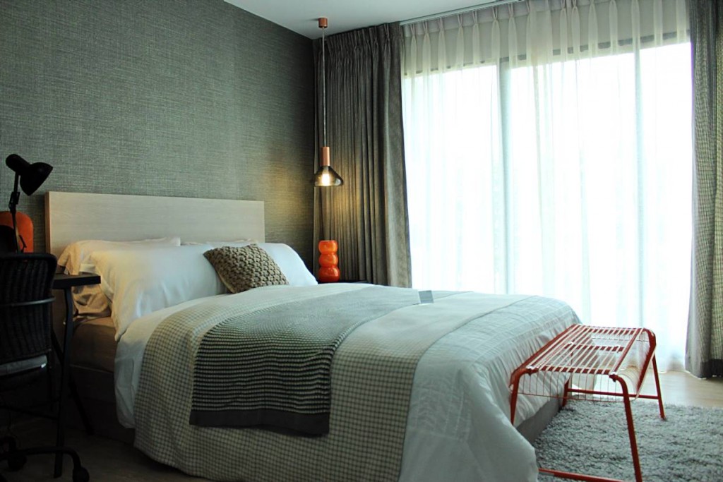 มุมมองภายในห้องนอนใหญ่ ซึ่งจะประกอบไปด้วย โต๊ะทำงาน ตู้เสื้อผ้า และชั้นวางทีวีแบบบิลท์อินอยู่ฝั่งปลายเตียง และระเบียงห้องด้านนอก