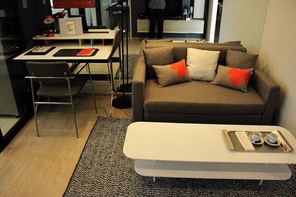 พื้นห้องนั่งเล่นปูด้วยไวนิลลายไม้ บริเวณนี้ประกอบไปด้วยโซฟาขนาด 2 ที่นั่ง มาพร้อมกับโต๊ะกาแฟ สีขาวสไตล์โมเดิร์น ขนาดพอกันกับโซฟา และโต๊ะเขียนหนังสือที่ให้มาเช่นกัน