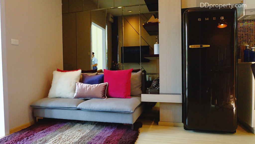 สำหรับผนังห้องจริงที่ได้จะเป็นผนังฉาบเรียบ ติดวอลล์เปเปอร์สีขาวตามมาตรฐานโครงการ งานบิลท์อินชั้นวางเป็นเพียงไอเดียในการแต่งห้องเท่านั้น ถ้าอยากให้พื้นที่วางโซฟาดูเต็มๆ สามารถนำโซฟาไซส์ขนาด 2 ที่นั่งมาวางได้ 