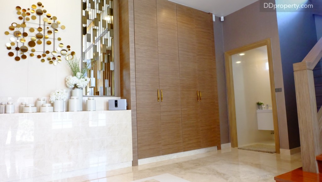 เมื่อเปิดประตูเข้ามาจะพบห้องน้ำของชั้น 1 ที่ตั้งอยู่ทางฝั่งขวามือติดกับบันไดทางขึ้น พื้นชั้นหนึ่งปูด้วยแกรนิตโต้, บ้านตัวอย่างบิลท์อินตู้วางรองเท้ามาให้ สำหรับบ้านเปล่า บริเวณนี้จะเป็นพื้นที่โล่งๆ แต่พื้นยังคงปูกระเบื้องแกรนิตโต้มาให้ ความสูงพื้นจรดเพดานส่วนนี้  2.8 เมตร