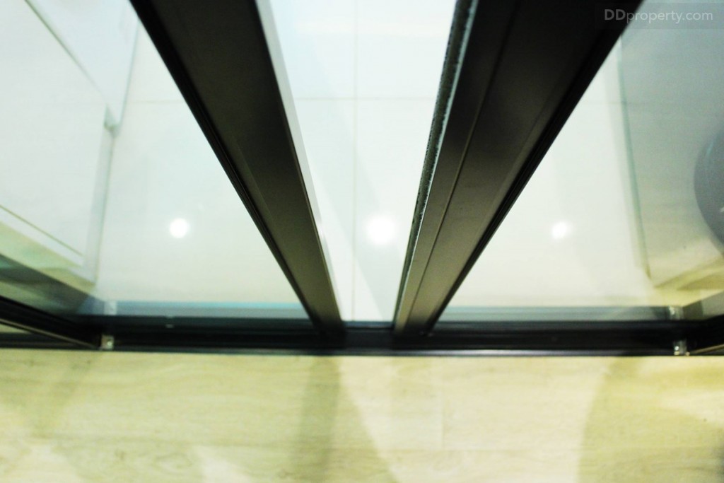 ห้องครัวกับห้องโถงกั้น ประตูกระจกบานเลือนขอบอลูมิเนียมสีดำ ช่วยป้องกันควันหรือกลิ่นจากการประกอบอาหาร ส่วนพื้นห้องโถ่งจะเป็นลามิเนตหน้า 8 มม.