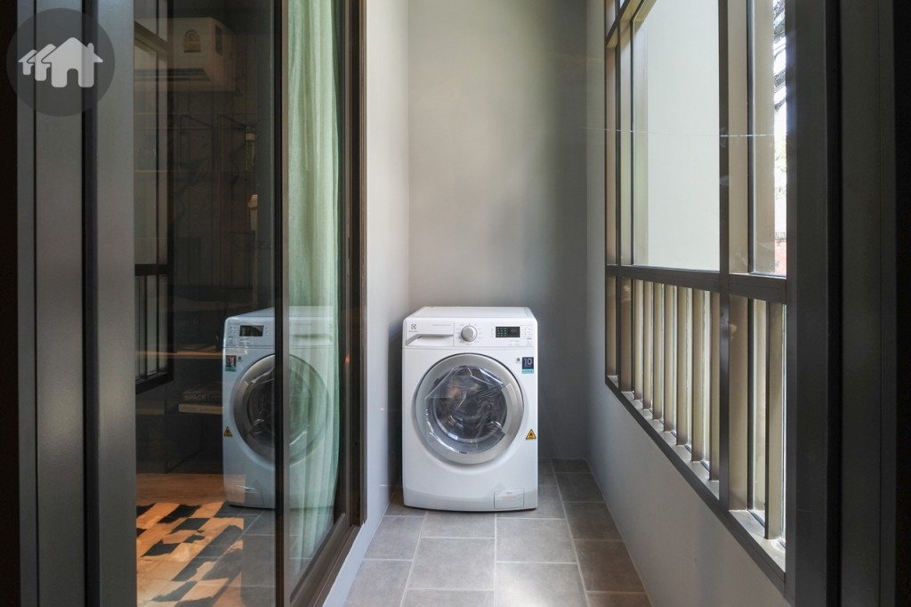 ห้องนั่งเล่นเชื่อมต่อกับระเบียงด้วยประตูบานเลื่อนแบบสลับเต็มบาน รับแสงธรรมชาติ ระเบียงกว้างประมาณ 1 เมตร พื้นปูกระเบื้องขนาด 30x30 เซนติเมตร วางเครื่องซักผ้าได้ โดยระเบียงด้านข้างกั้นเป็นกำแพงทึบป้องกันฝนสาดได้ รั้วระเบียงสูงประมาณ 1.10 เมตร