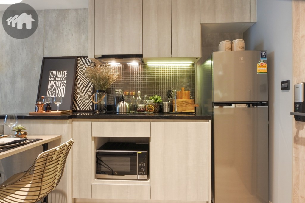 ตรงข้ามเป็นห้องครัวพร้อมตู้บิวท์อินบน-ล่าง มีพื้นที่วางตู้เย็น และเตาไมโครเวฟ ตัว Top เคาน์เตอร์ครัวด้านล่างเป็นหินควอชซ์สีดำ พร้อมอ่างล้างจาน เตาไฟฟ้าฐานเซรามิก 2 หัว และเครื่องดูดควันของ Hafele