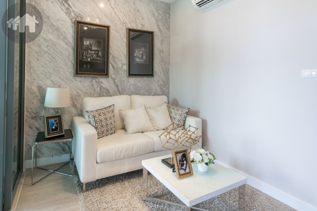 ห้องนั่งเล่น ตกแต่งอย่างเรียบง่าย มีพื้นที่วางโคมไฟ หรือของตกแต่ง และโต๊ะกลาง ระยะห่างจากผนังถึงประตูกระจกบานเลื่อนอีกด้านกว้างประมาณ 2.30 เมตร