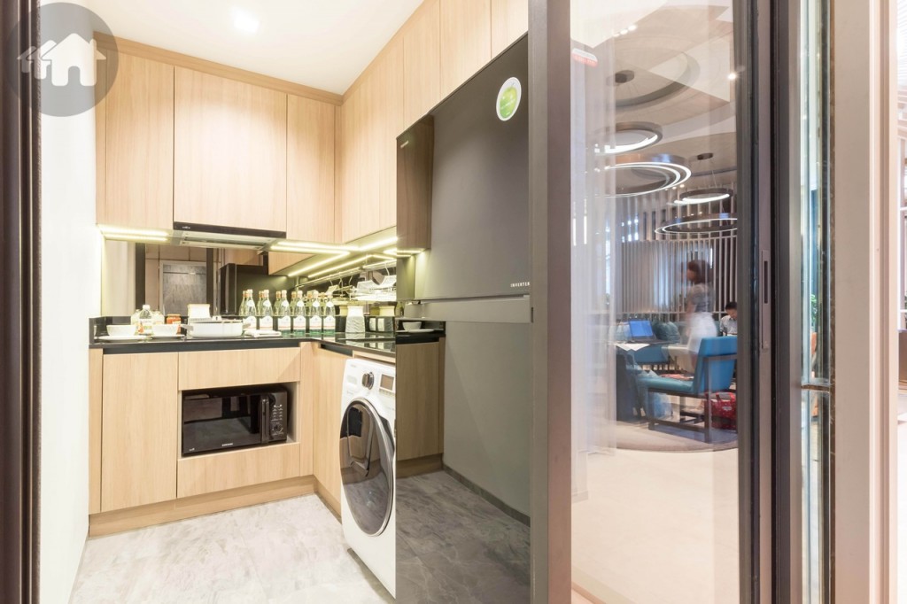 ด้านขวาเป็นห้องครัวกั้นด้วยกระจกบานเลื่อนแบบ 3 ตอนเป็นสัดส่วน เหมาะสำหรับคนที่ชอบทำครัวแบบจริงจัง พร้อมตู้บิลท์อินบน-ล่าง อ่างล้างจาน เตาไฟฟ้าฐานเซรามิกและเครื่องดูดควันของ MEX ผนังครัว Back splash เป็นกระจก มาพร้อมที่วางจานแขวนบนผนัง ทางเดินกว้างประมาณ 1 เมตร พื้นปูกระเบื้องลายหินขนาด 60x60 เซนติเมตร