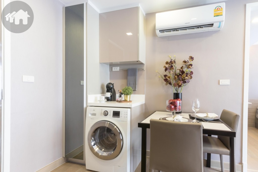 On the opposite side of the kitchen, there are a tall shoes cabinet, a shelf with a washing machine (from Samsung) underneath, and a dining table with two chairs and featured table ware including wine and coffee glasses and a kettle.