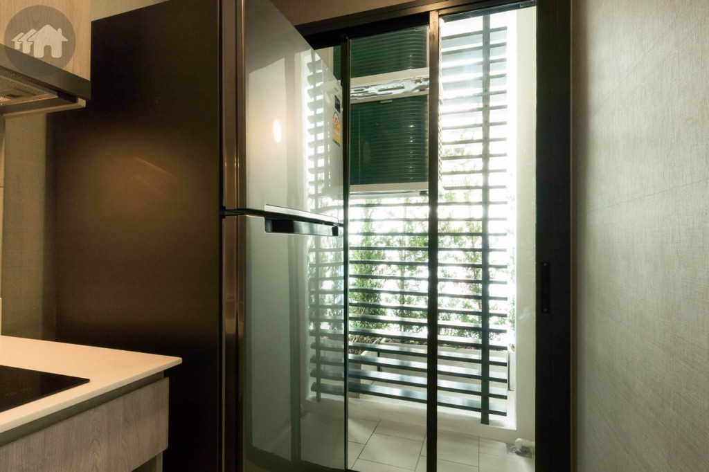 ด้านข้างตู้ครัวมีพื้นที่ว่างประมาณ 85 เซนติเมตร วางตู้เย็นขนด 13.5 คิว ได้สบาย ๆ มีประตูกระจก Laminated Glass บานเลื่อน 3 ตอน เชื่อมต่อกับระเบียงกว้างประมาณ 80 เซนติเมตร ยาวประมาณ 1.65 เมตร ขอบประตูยกพื้นสูงประมาณ 10 เซนติเมตร พื้นปูกระเบื้องขนาด 30x30 เซนติเมตร ด้านบนติดตั้งคอมเพรสเซอร์เครื่องปรับอากาศ สูงจากพื้นประมาณ 1.40 เมตร