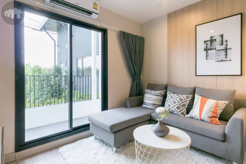 ตรงข้ามเป็นโซฟารูปตัวแอล และโต๊ะกาแฟ เปิดรับวิวด้วยประตูกระจกบานเลื่อนแบบสลับ ขอบประตูยกสูงประมาณ 15 เซนติเมตร