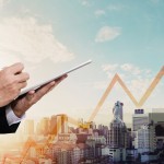 Businessman working digital tablet, with panorama city and raising arrow