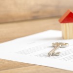 Silver house key lying on a contract of house sale