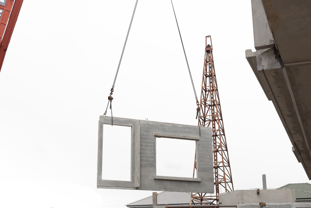 Construction site crane is lifting a precast concrete wall panel to installation building.