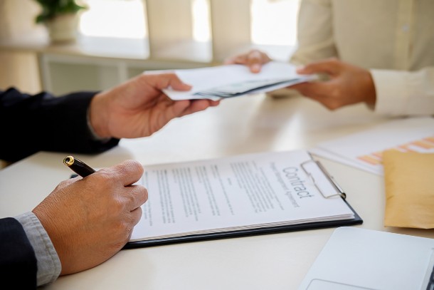 Man signing a debt contract, while receiving a document and stack of bills