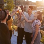 Friends make a toast at a rooftop party, backlit by sunlight