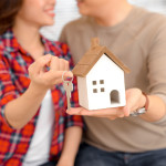 Happy couple holding keys to new home and house miniature - real estate concept