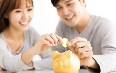 Happy young Couple Inserting Coin In Piggybank